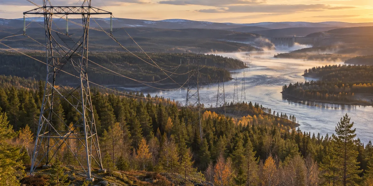Kraftledning genom norrländsk skog längs en älv med vattenkraftsdamm i fjärran
